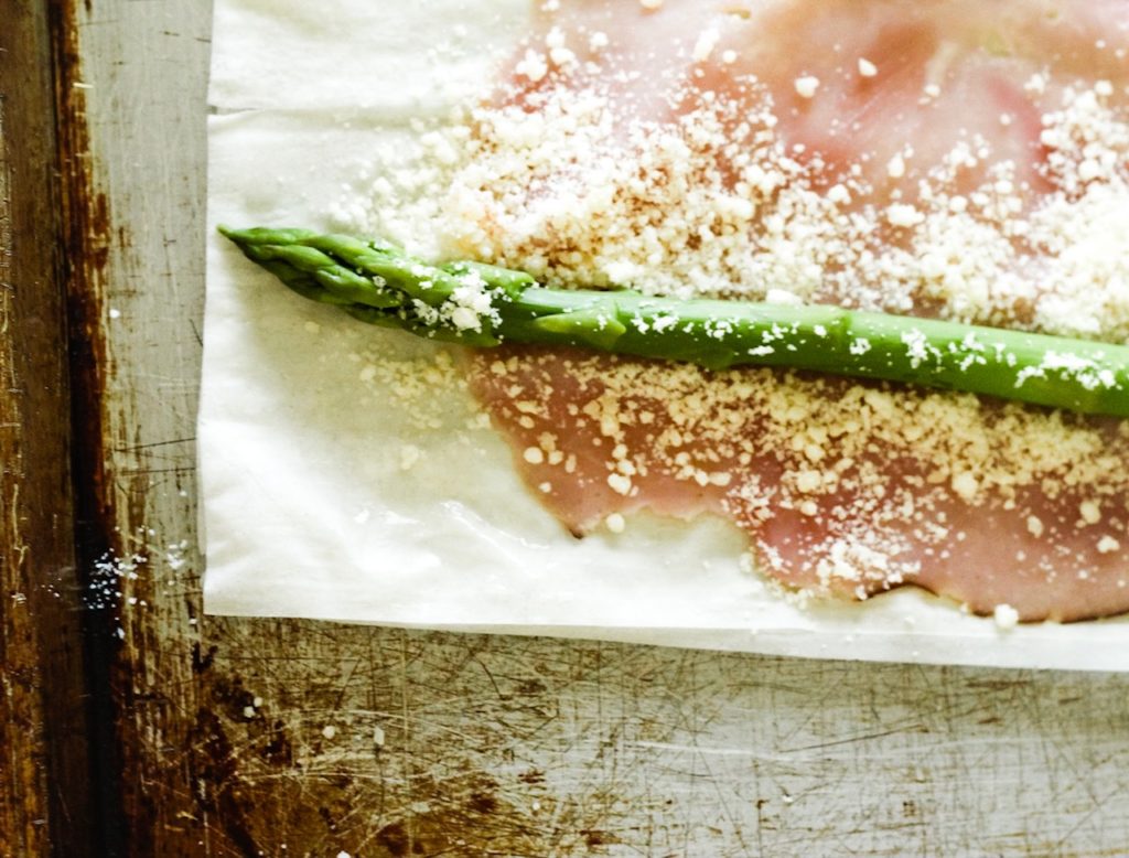 Close-up of a parmesan asparagus wrap ready to be rolled. Asparagus on top of ham and phyllo dough, sprinkled with parmesan cheese.